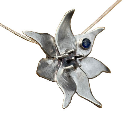 Silver flower-shaped pendant with a blue gemstone on white background